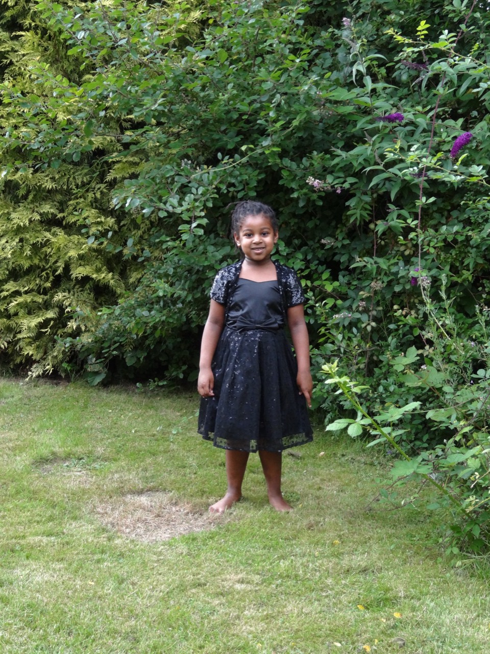 A young Alanna standing in a black dress among the garden greenery.