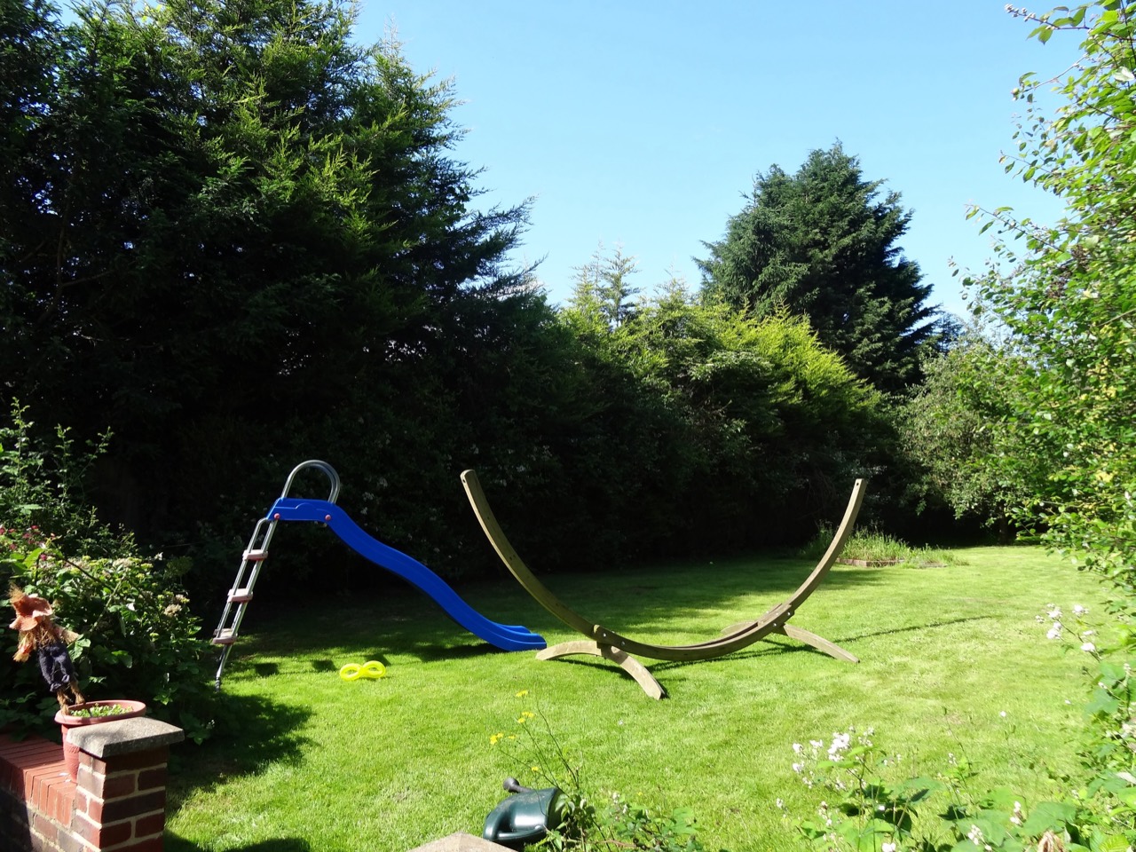 The blue slide and wooden hammock frame surrounded by the garden.