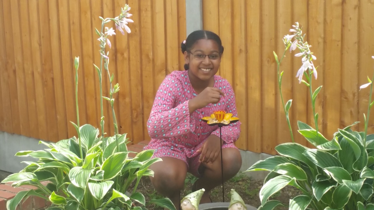 A smiling young Alanna surrounded by flowers in the garden.