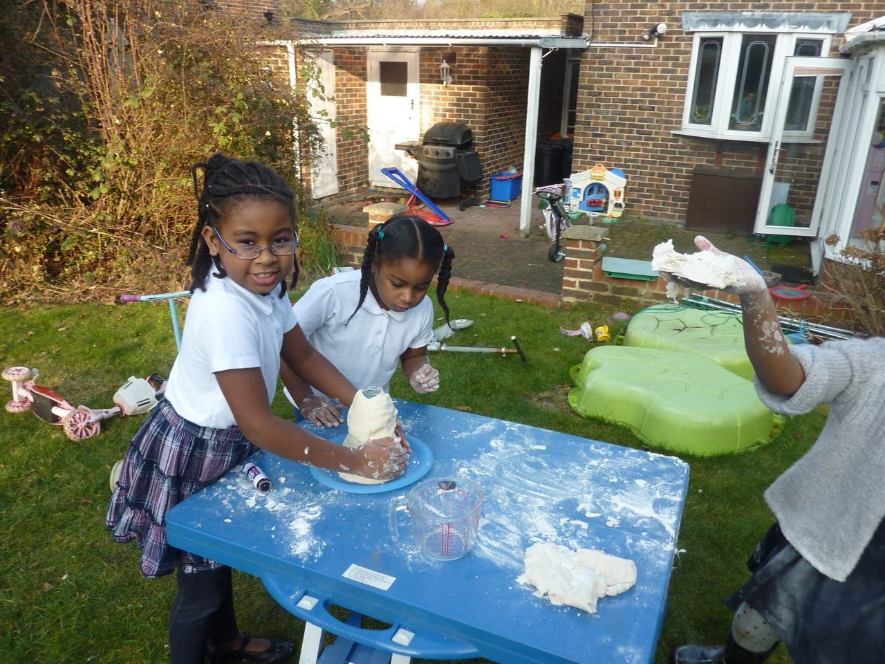 Children making and exploring dough at a blue table outside.