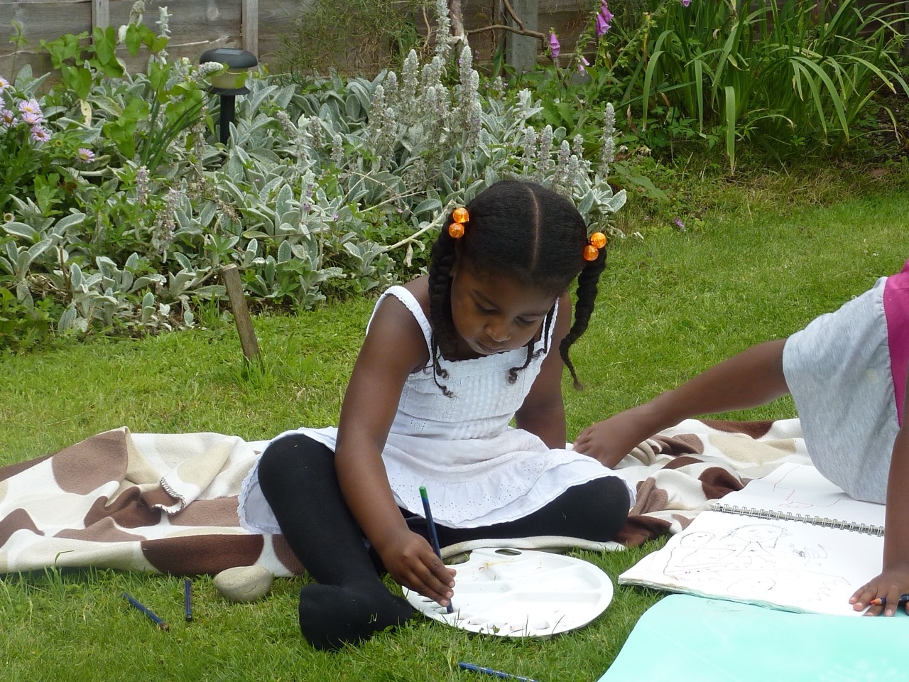 A child painting outdoors on a blanket in the garden.