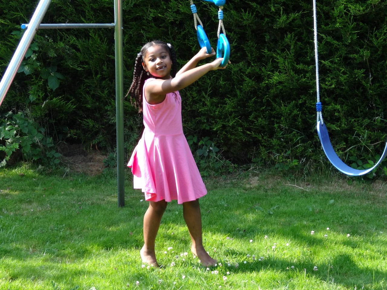 A child in a pink dress playing beside the garden swings.
