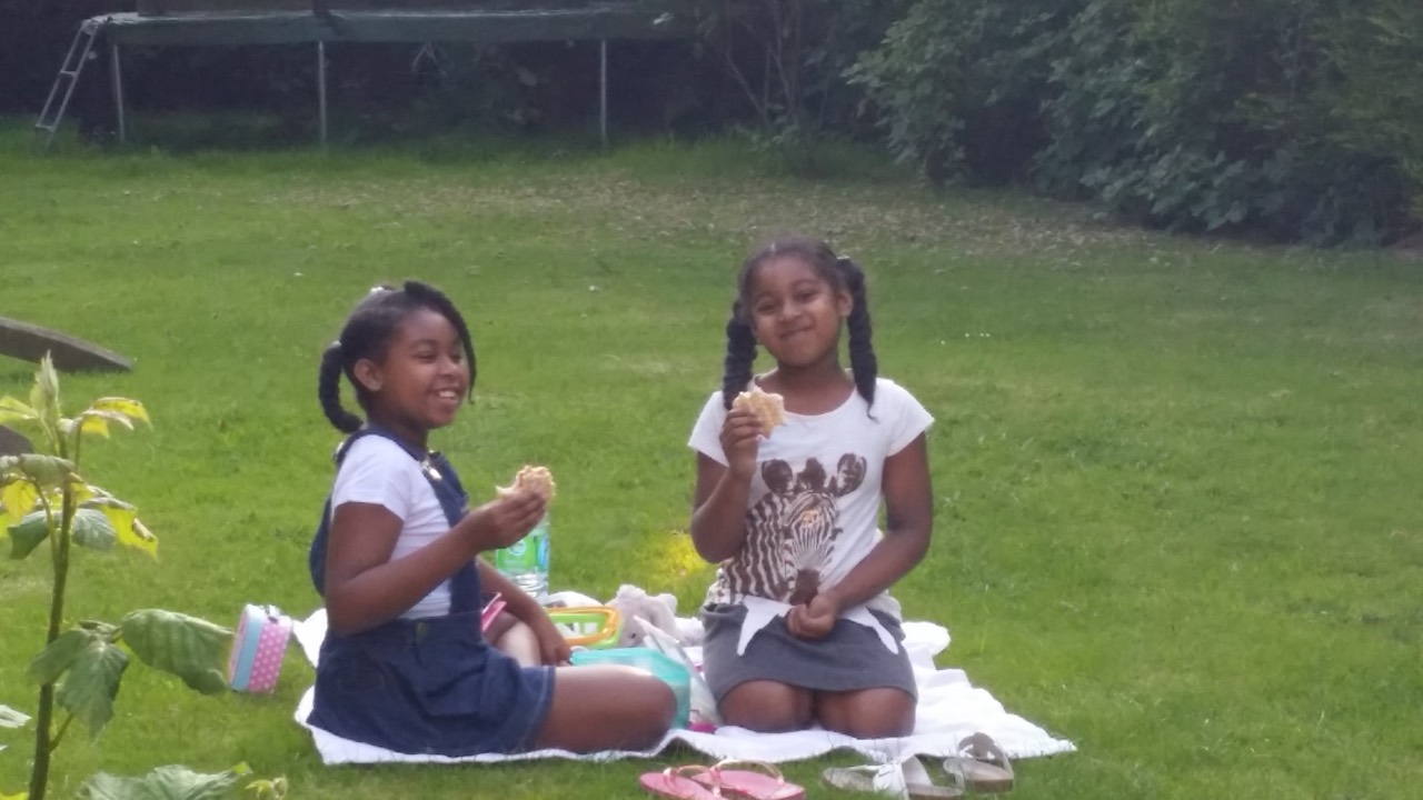 Two sisters sharing lunch on a picnic blanket in the garden.