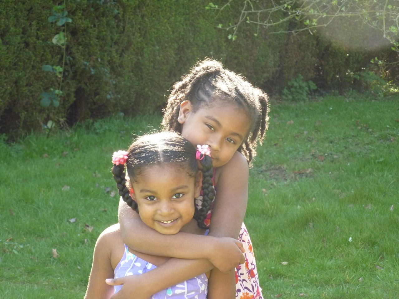 Two sisters hugging in the sunlight in their childhood garden.