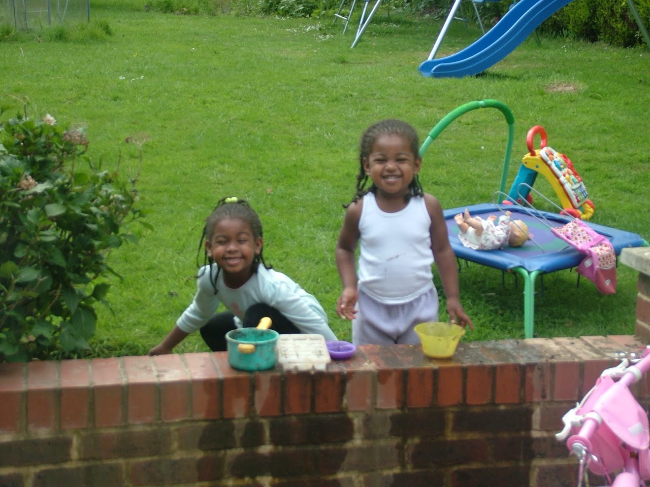 Two young sisters playing together beside the garden wall.