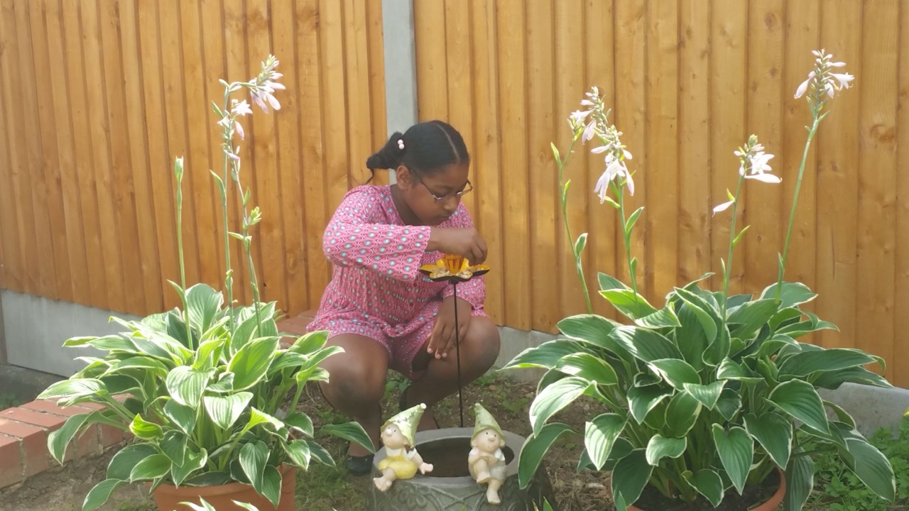 A young Alanna tending a flower ornament among plants in the garden.